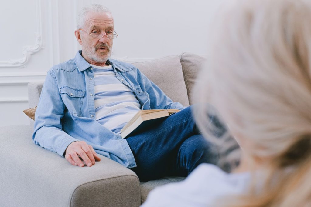 Therapeutin im ruhigen Gespräch mit einem älteren Patienten auf dem Sofa