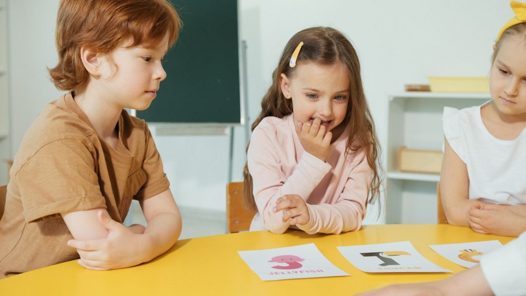 Drei Kinder sitzen gemeinsam am Tisch und arbeiten mit Übungskarten